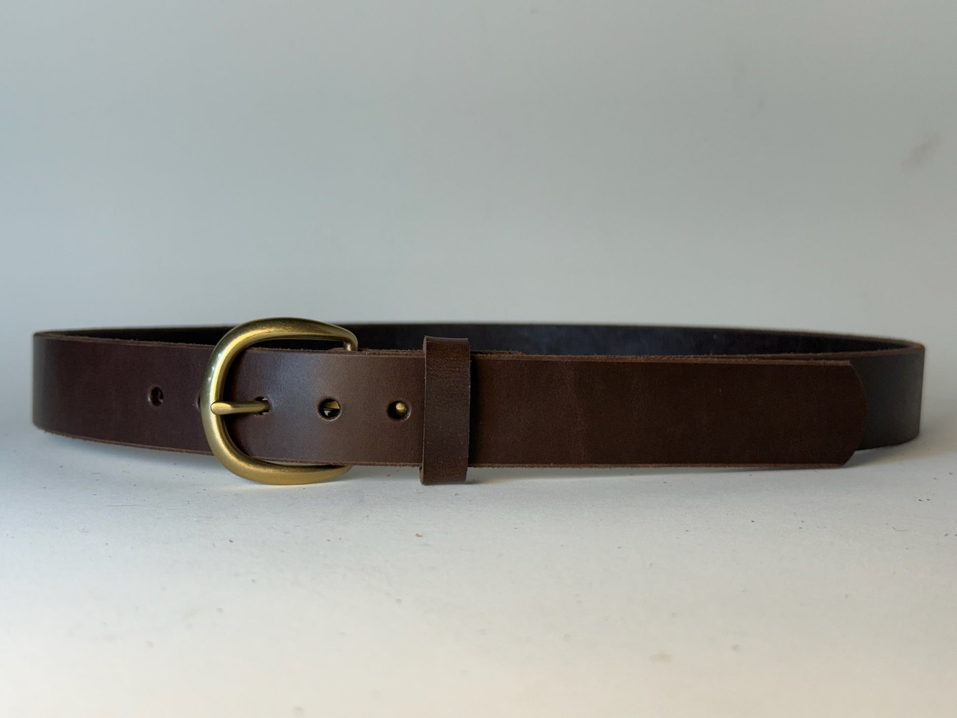 Dark brown leather belt with a gold buckle on a gray background