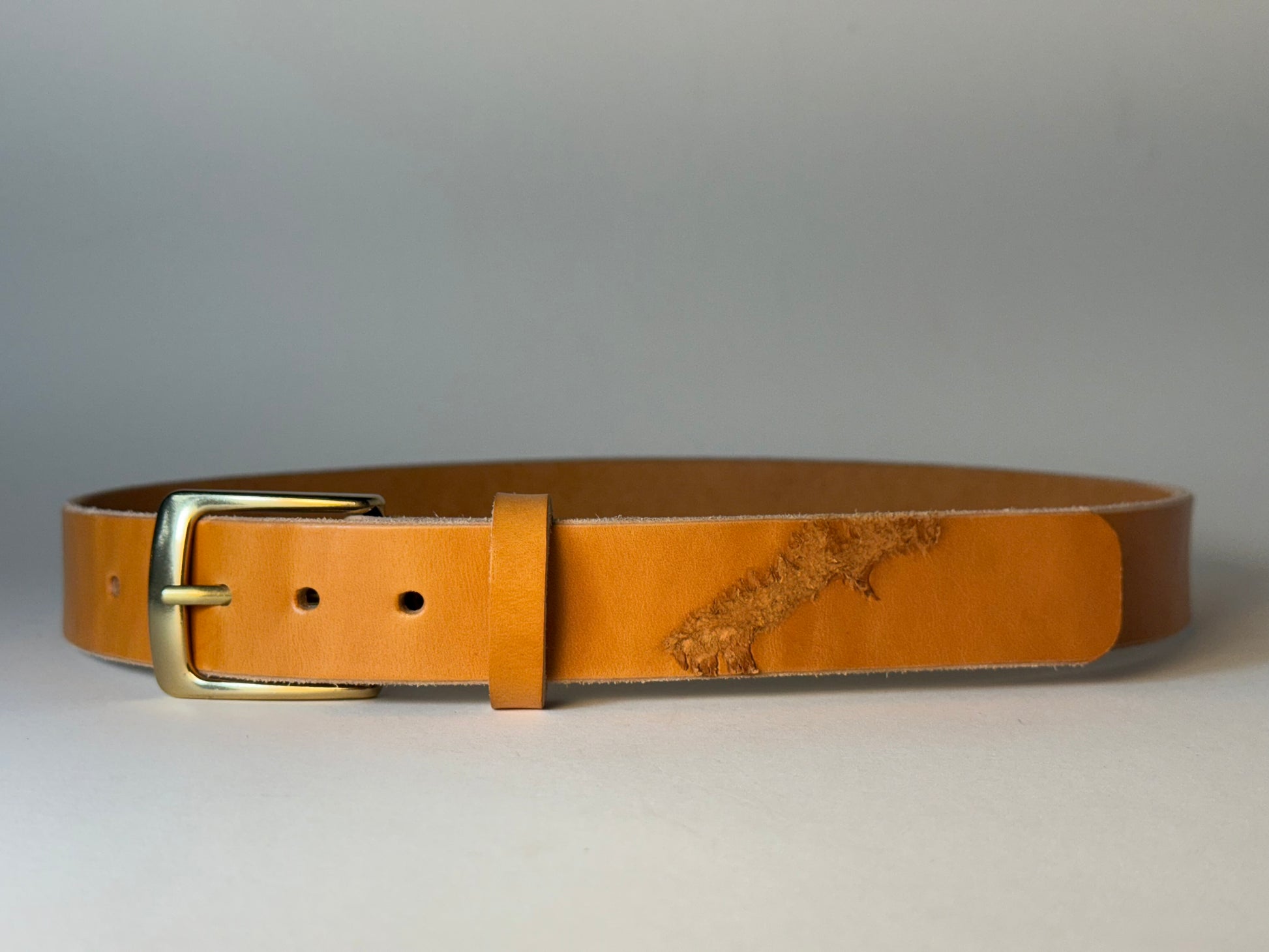 Golden honey leather belt with a gold buckle on a light gray background