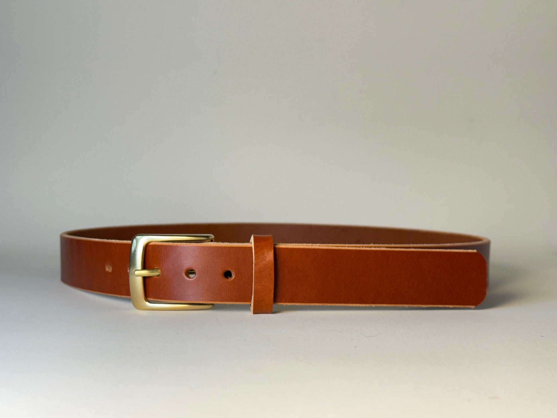 Reddish brown leather belt with a silver buckle on a gray background