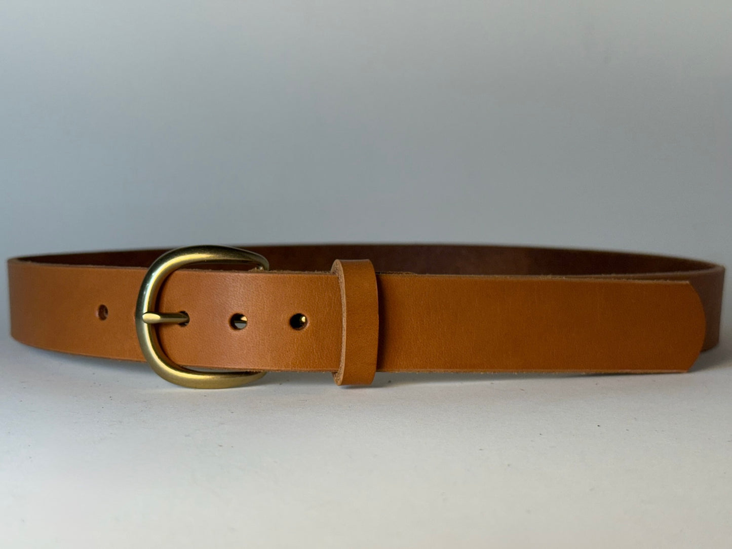 Tan leather belt with a gold buckle on a white background