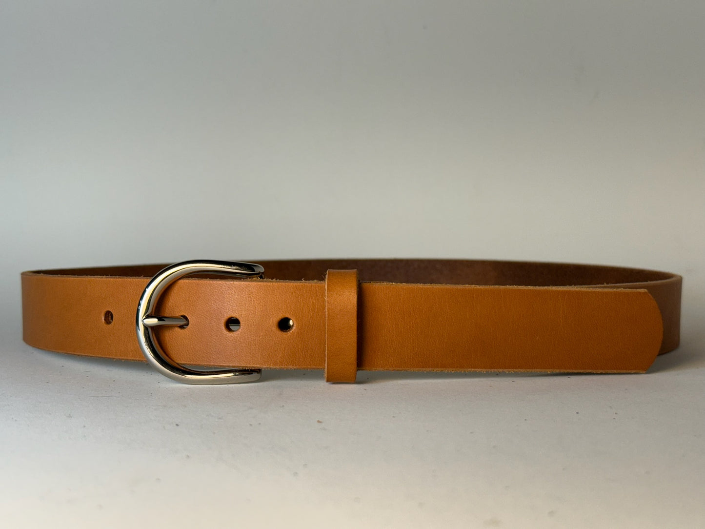 Tan leather belt with a silver buckle on a light gray background