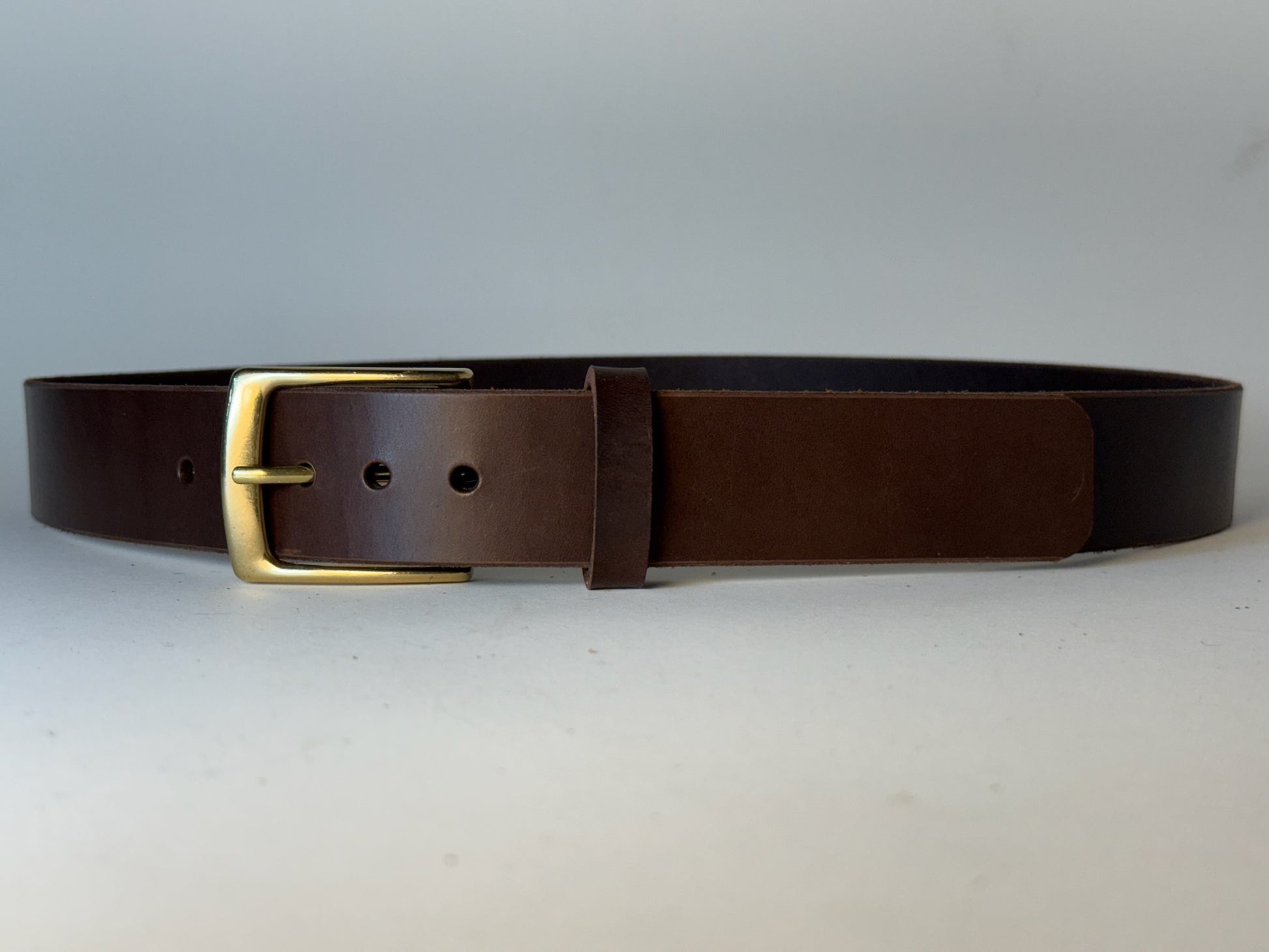 Dark brown leather belt with a gold buckle on a gray background