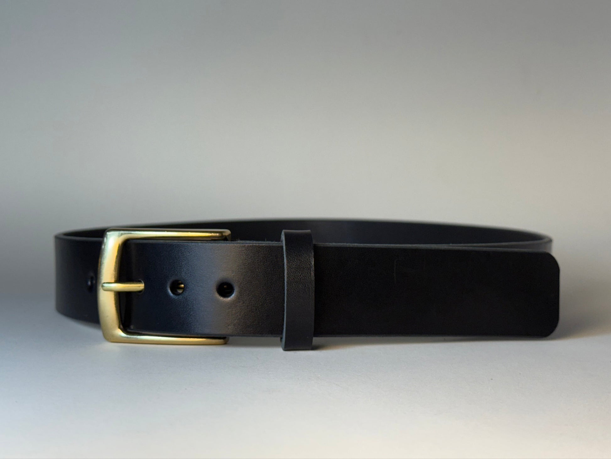 Black leather belt with a gold buckle on a gray background