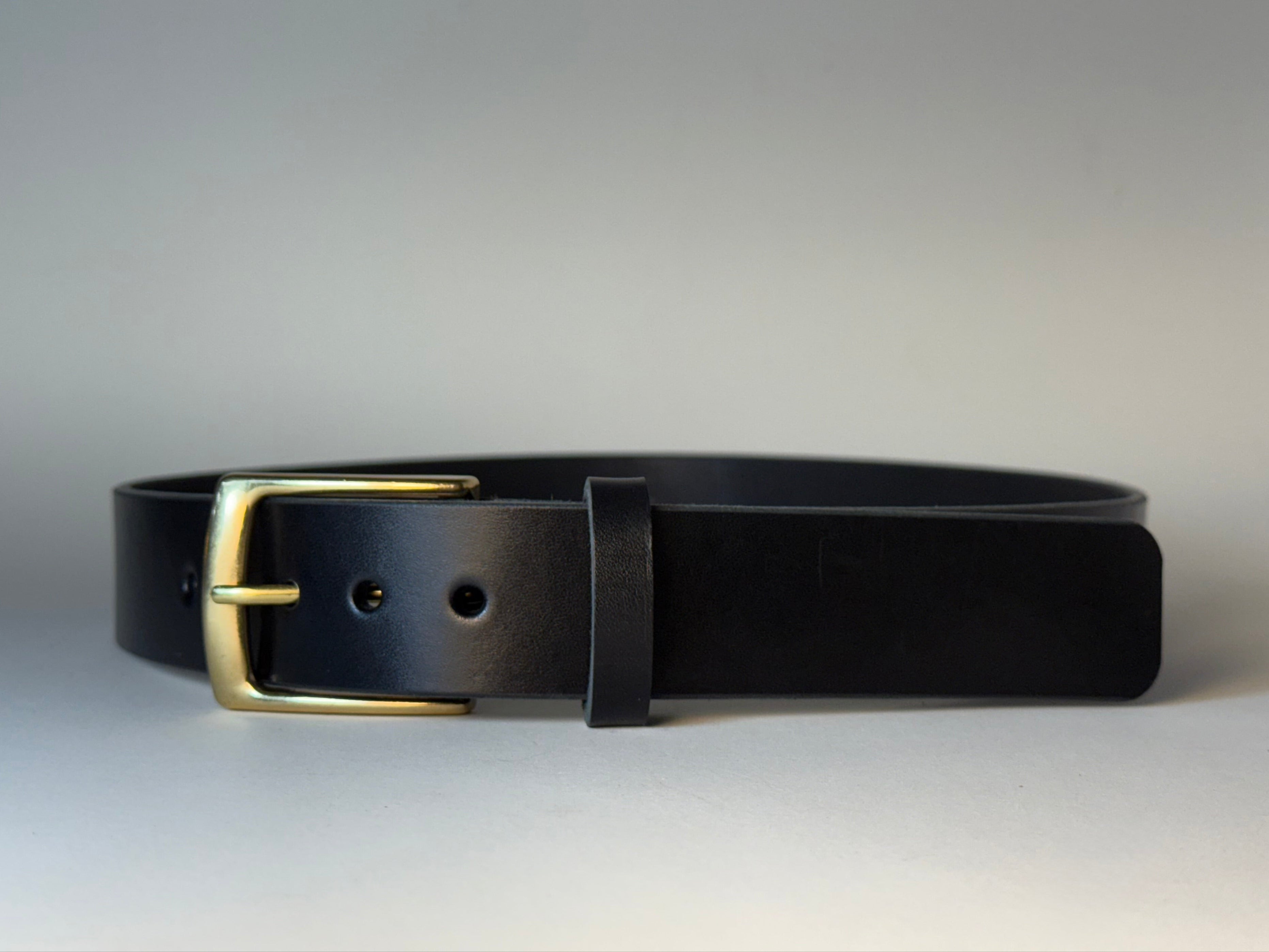 Black leather belt with a gold buckle on a gray background