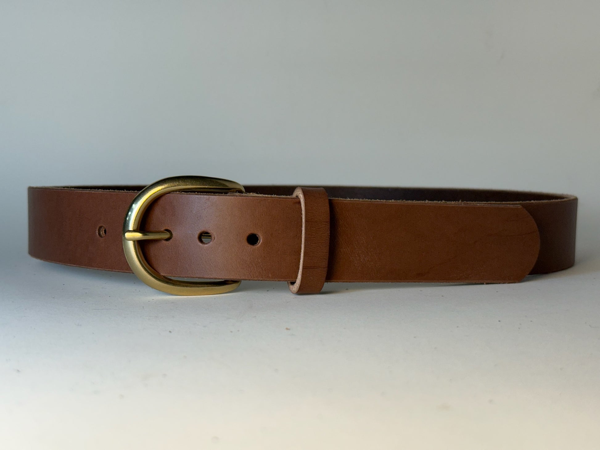 Brown leather belt with a gold buckle on a light gray background