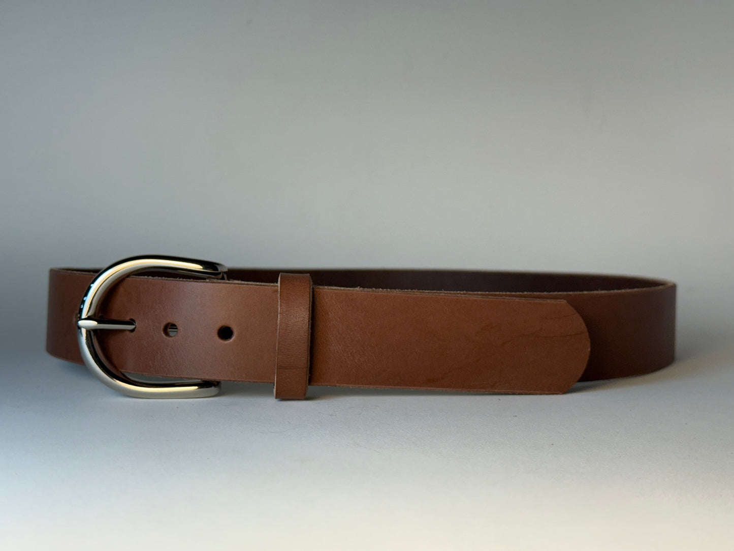 Brown leather belt with a silver buckle on a gray background