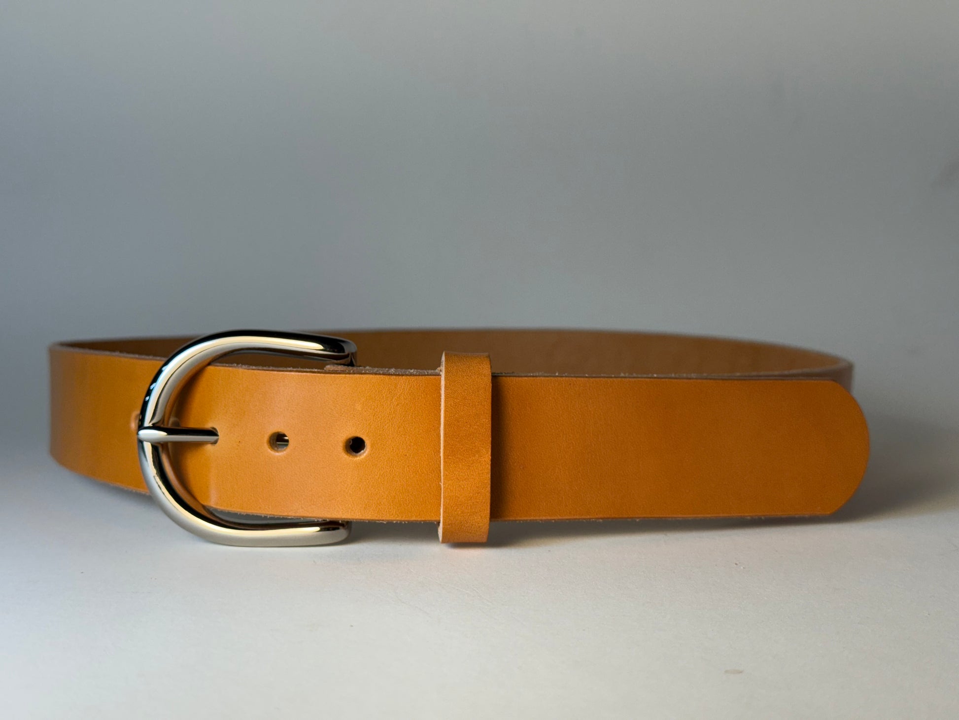 Golden honey leather belt with a silver buckle on a light gray background
