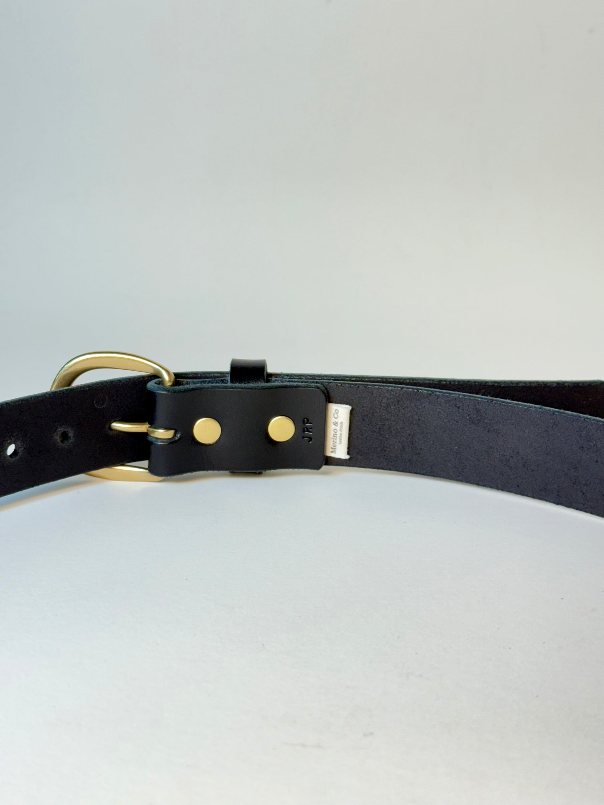 Black leather belt with gold hardware on a light gray background