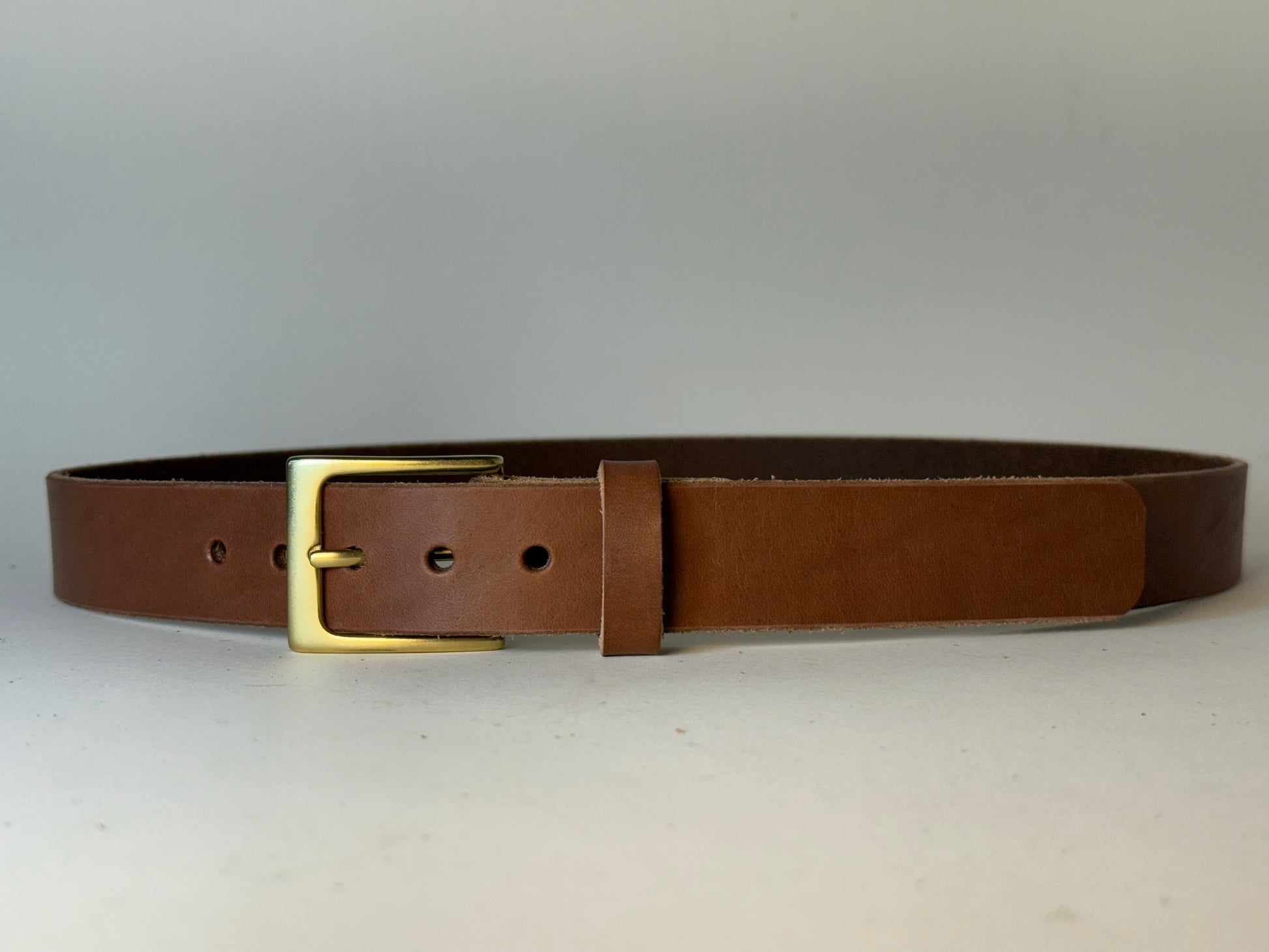 Light  brown leather belt with a silver buckle on a gray background