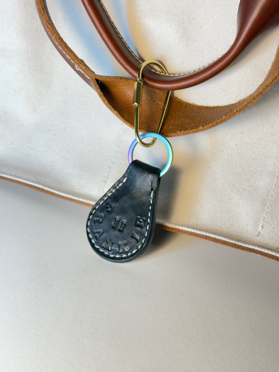 Close-up of a brown leather strap with a black leather tag and gold clasp on a beige background.