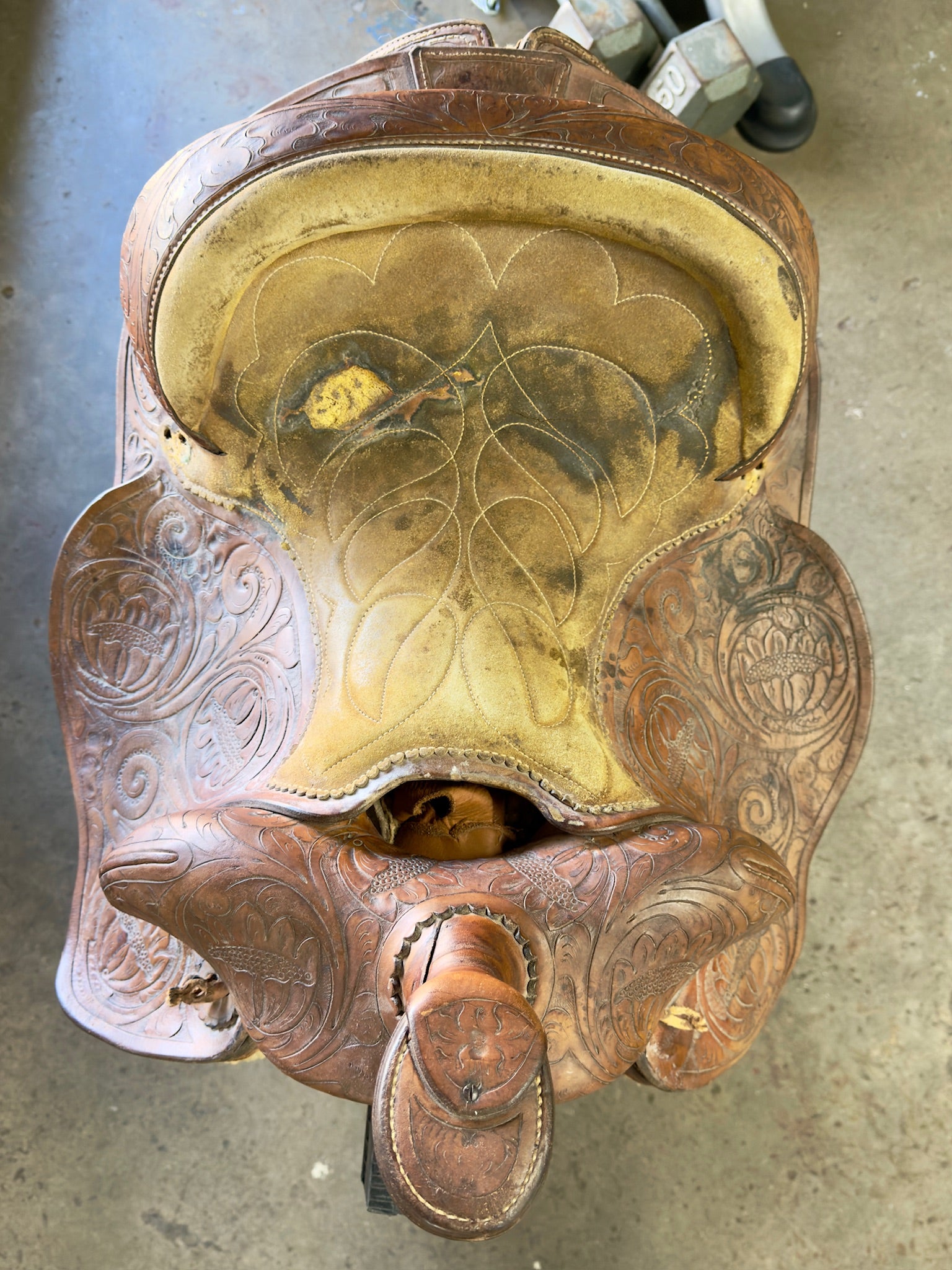 Close-up of a detailed leather saddle with floral patterns on a concrete floor.