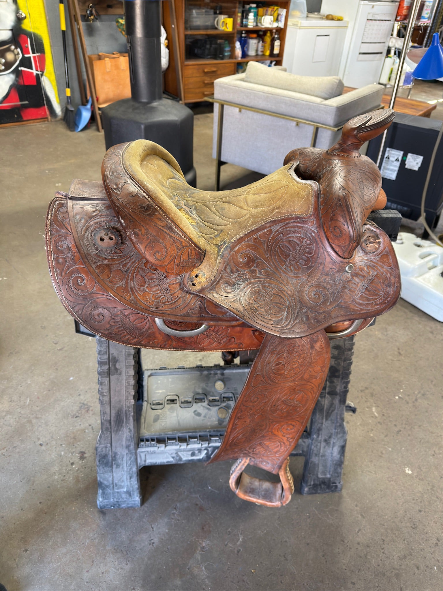 Brown leather saddle with intricate designs on a wooden pallet in an indoor setting.