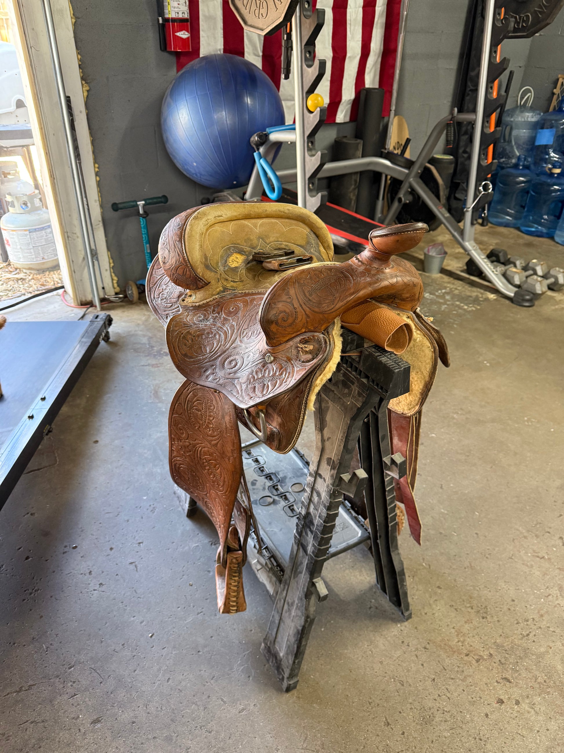 Brown leather saddle on a metal surface with tools and equipment in the background