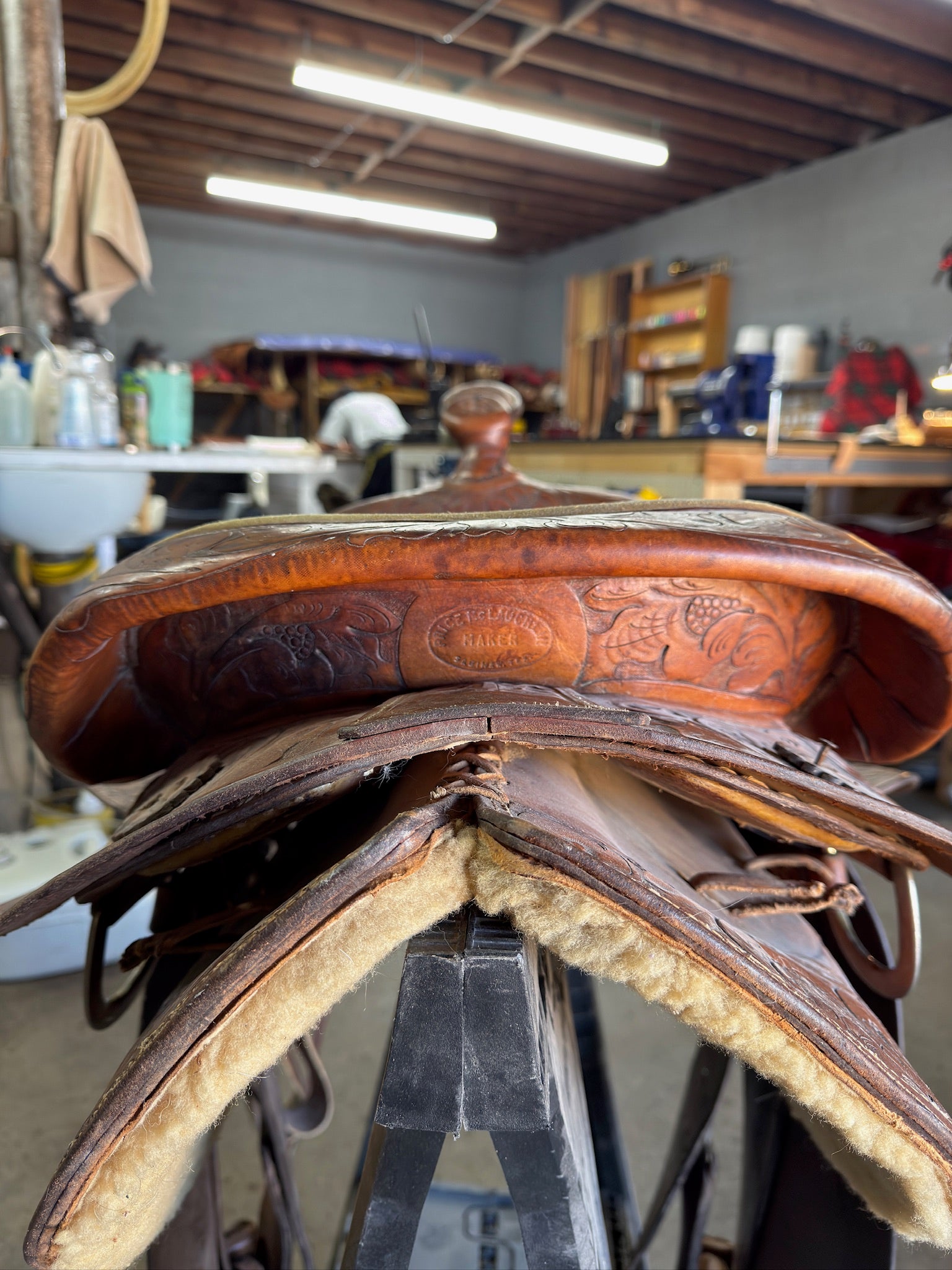Brown leather saddle with intricate designs on a stand in a workshop setting.