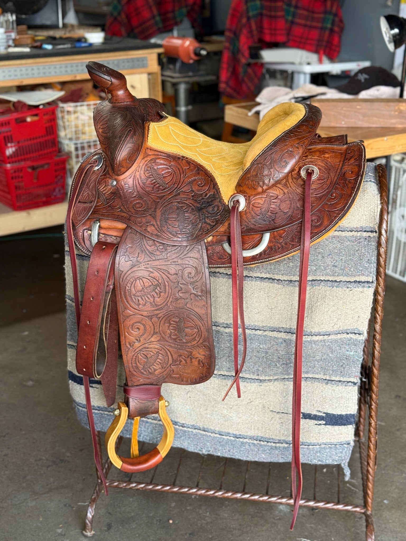 Brown leather saddle with intricate designs on a saddle blanket in a workshop setting.