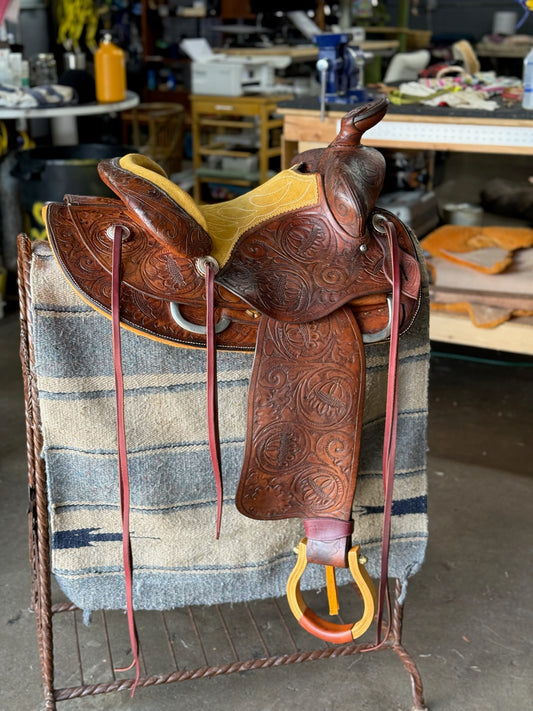 Brown leather saddle with intricate designs on a stand in a workshop setting