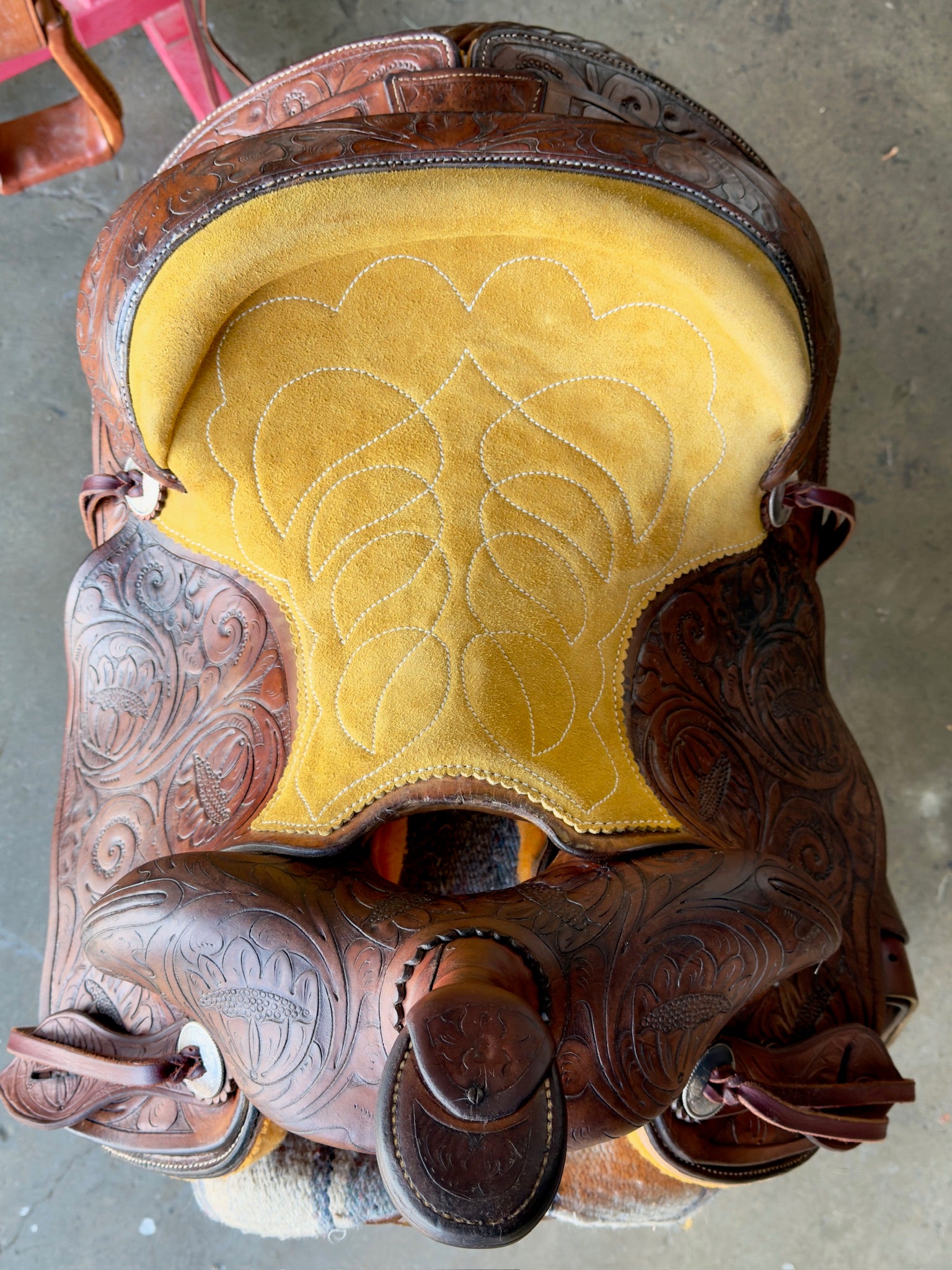 Close-up of a brown leather saddle with yellow seat pad on a concrete floor.
