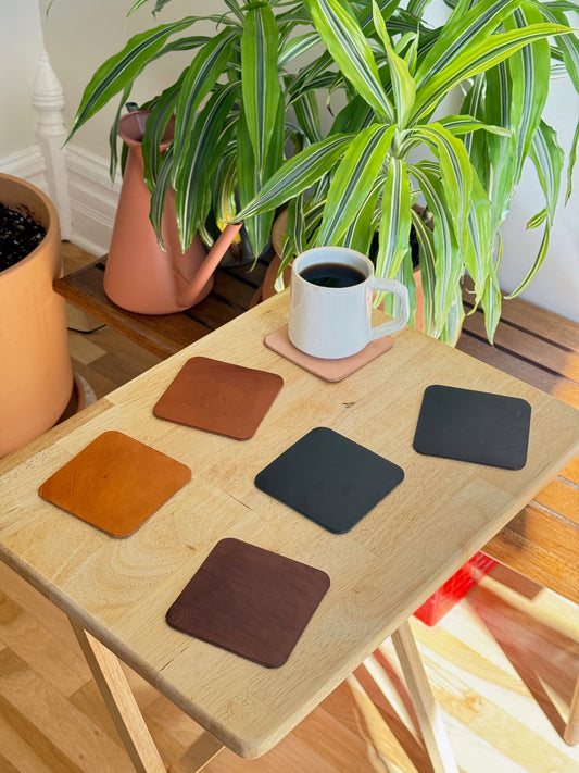 Wooden table with coasters and a cup of coffee, next to a potted plant
