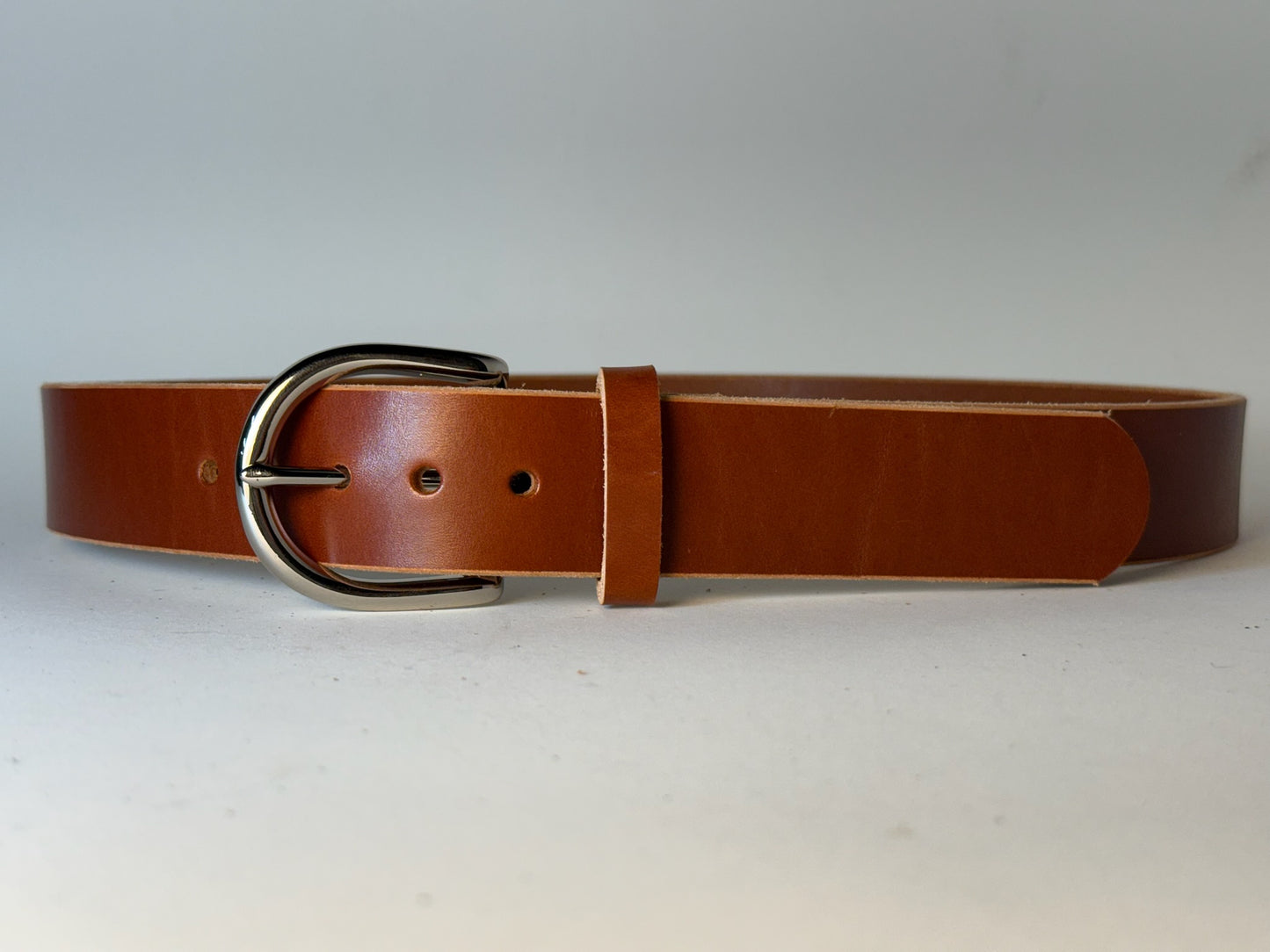 Reddish brown leather belt with a silver buckle on a gray background